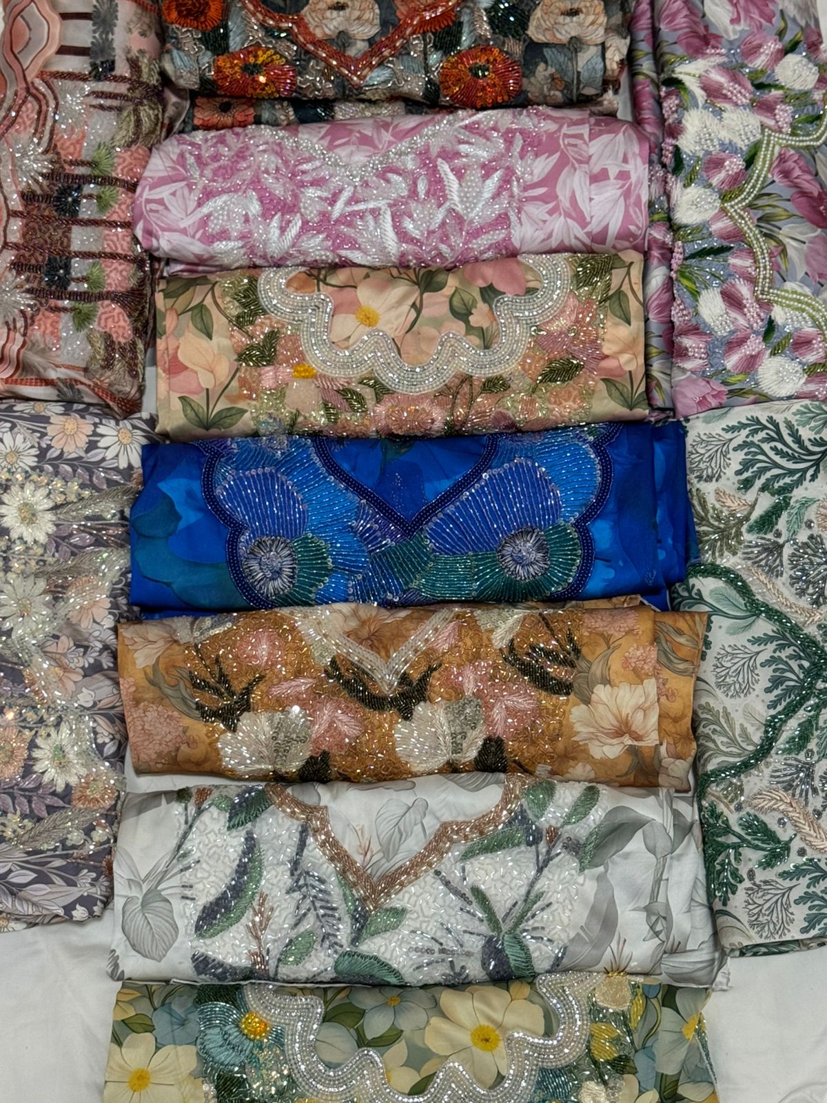 Stack of colorful embroidered fabric rolls with floral and abstract patterns.
